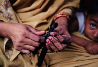 A child looks on while his mother, a home-based worker, cuts slipper straps outside their home in Delhi, India.