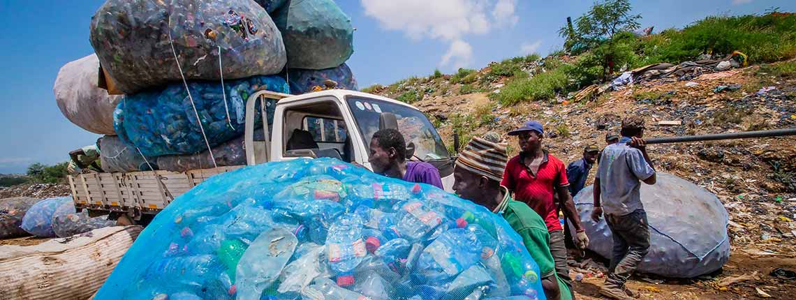 A group of informal workers collecting and transporting used plastic bottles on an open field