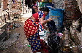 A resident of Savda Ghevra washing clothes in the narrow lane outside her home